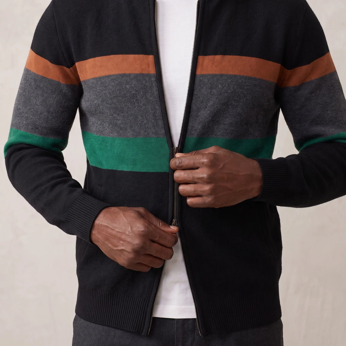 Man zipping up the green block stripe knit cardigan over a white tee