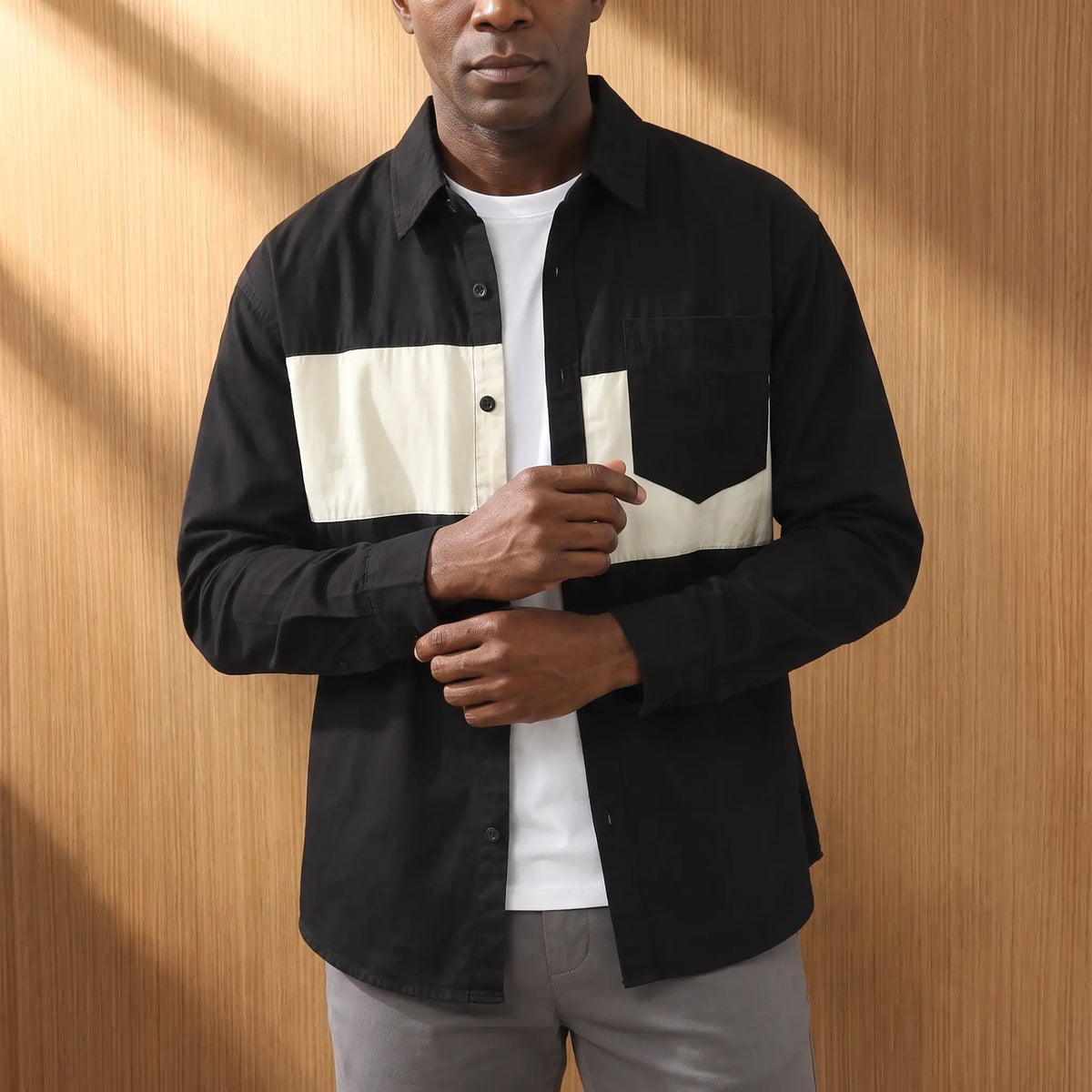 Man wearing a black chest band shirt open over a white tee with grey chinos