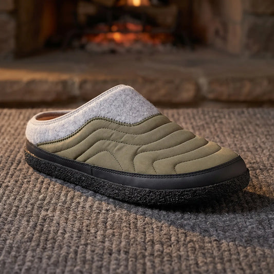 Men's green quilted backless slipper with felt collar and dark speckled sole on a wool rug by a fireplace