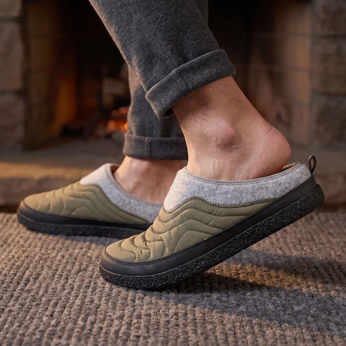 Man stepping into green quilted slippers by a fireplace