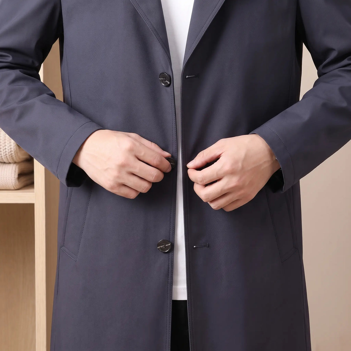 Man fastening the front button of the navy Flap Pocket Coat worn over a white tee