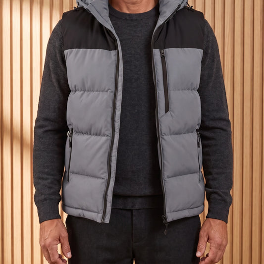 Men's grey hooded puffer vest with black yoke, worn open over a charcoal knit