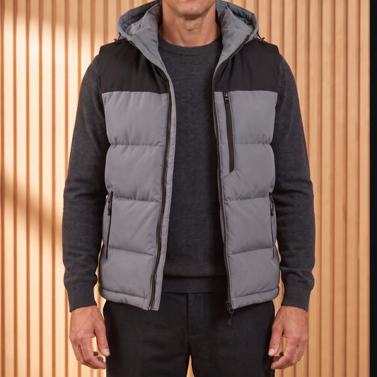 Men's grey hooded puffer vest with black yoke, worn open over a charcoal knit