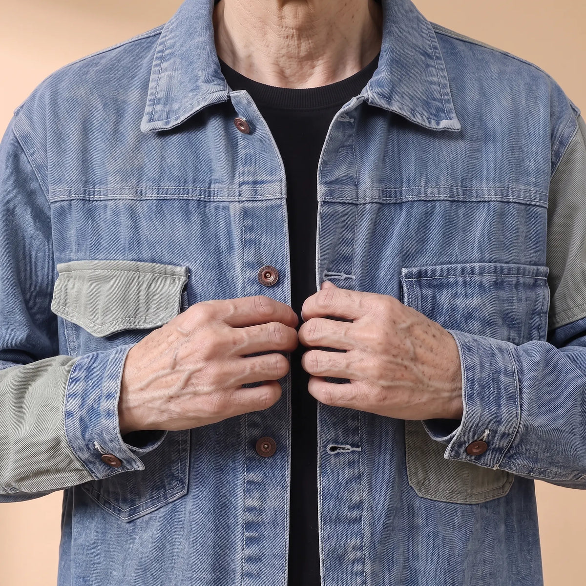 Older man fastening a copper shank button on the panelled denim jacket