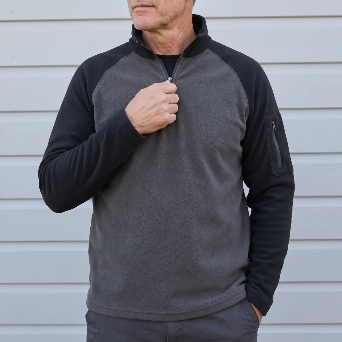 Man wearing the RAGLAN ZIP FLEECE in black, pulling up the quarter zip
