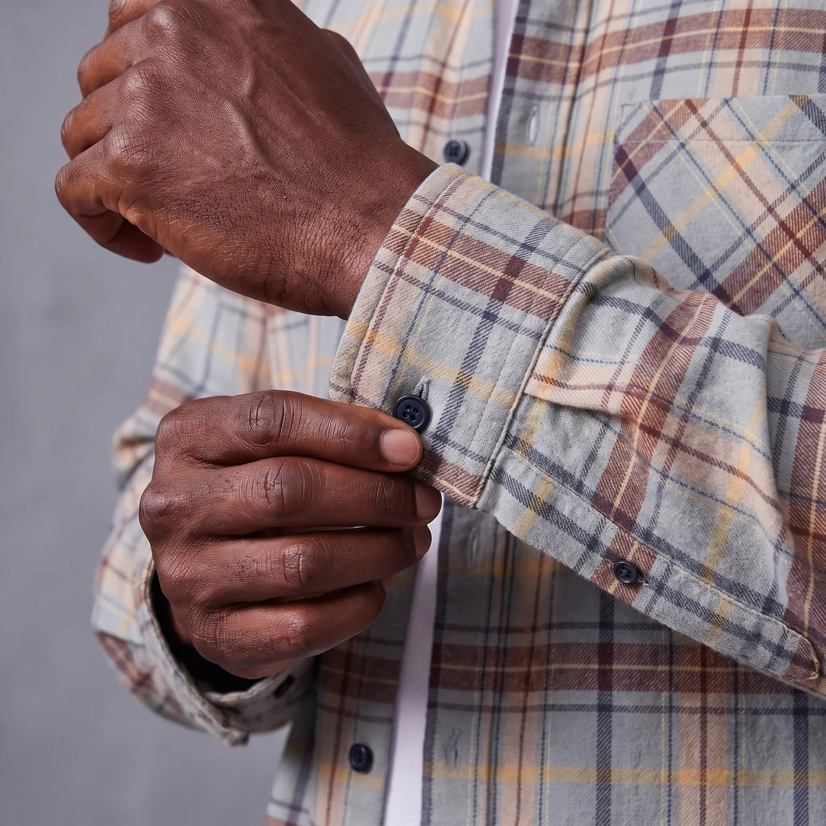 Older man fastening the cuff button on the plaid flannel shirt