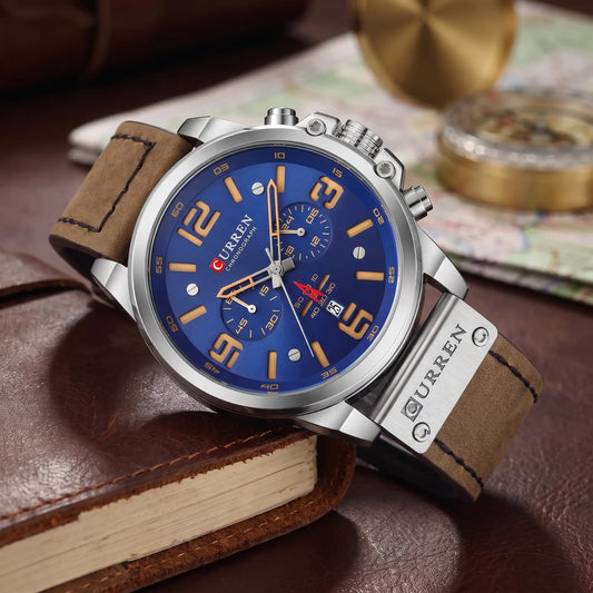Silver chronograph watch with blue dial and brown leather strap draped over a leather journal