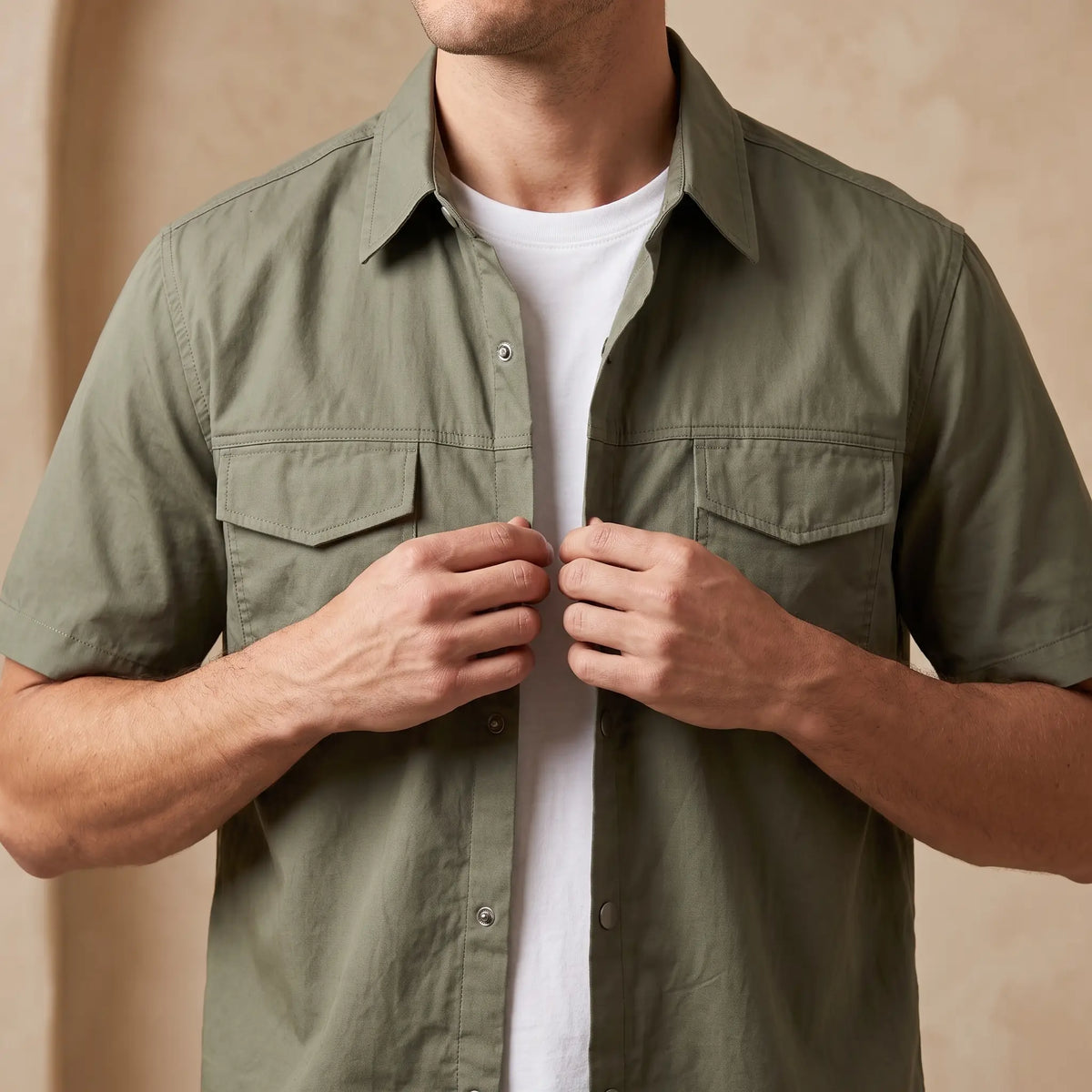 Man wearing the green short sleeve utility shirt over a white tee and buttoning the front