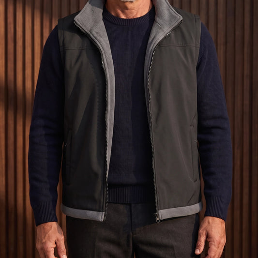 Men's black softshell vest with grey fleece lining, worn open over a navy sweater