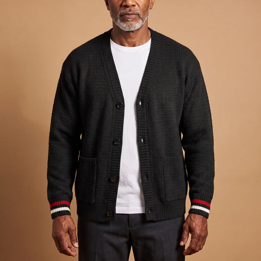Man wearing the Stripe Cuff Cardigan in black, a textured knit V-neck cardigan with red and white striped cuffs, worn open over a white tee