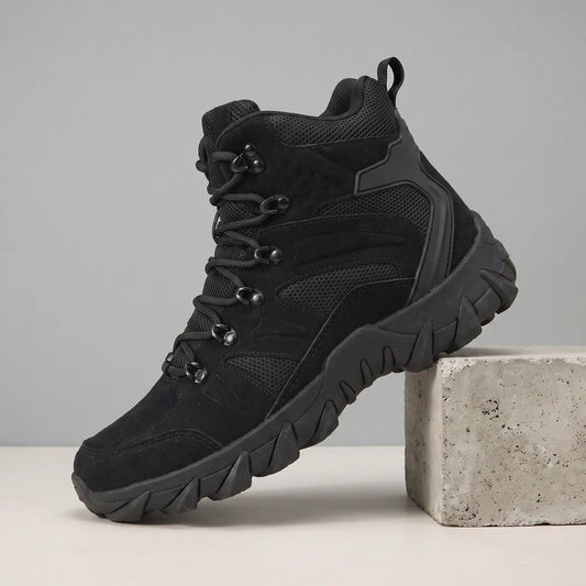 Soft Suede Hikers in black, a mid cut suede and mesh boot with fabric lace loops and a toothed sole, on a concrete block