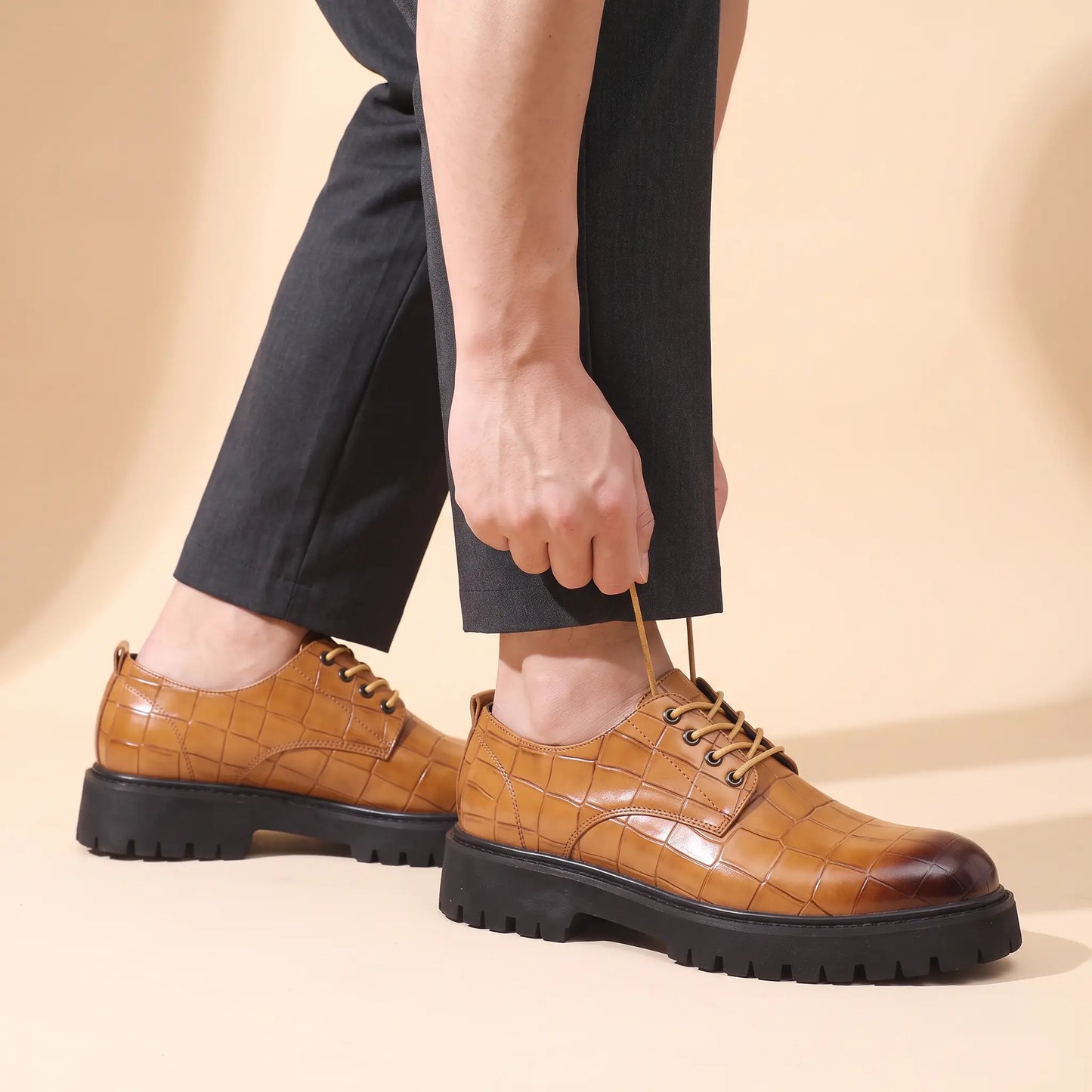 Man adjusting a lace while wearing the tan Square Scale Derby with charcoal trousers