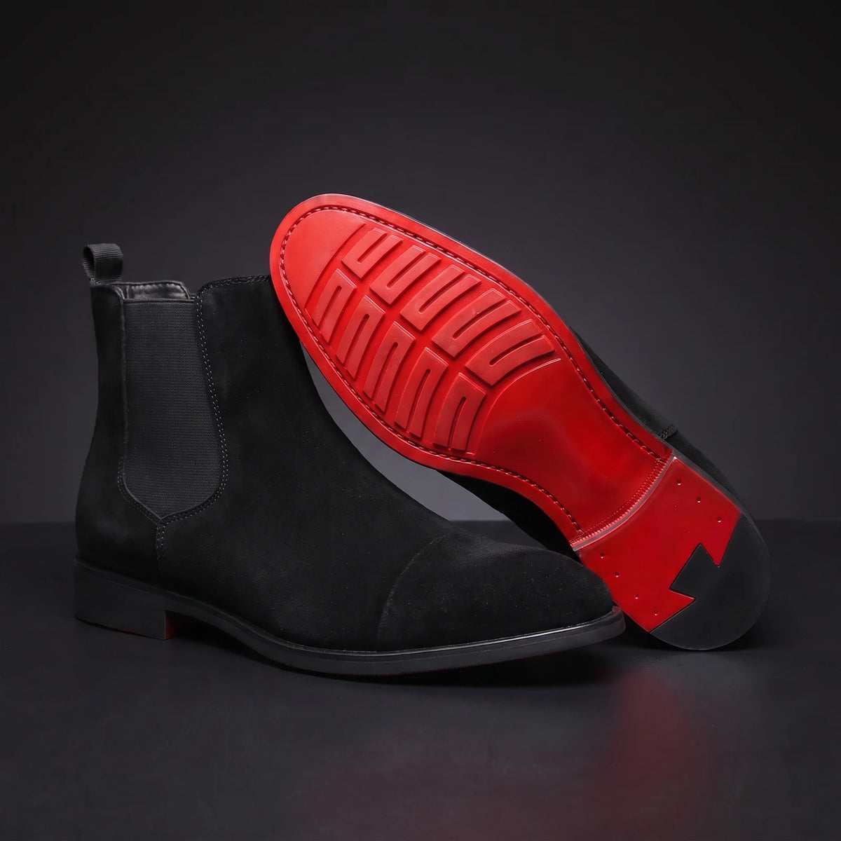 RED SOLE BOOTS matte black Chelsea boot propped toe-up showing the detailed red lugged sole, dark charcoal scene