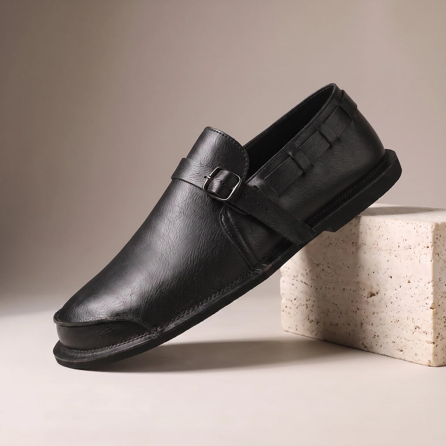 CLASSIC SLIP-ON LOAFERS black leather slip-on loafer with vamp strap on a travertine studio block