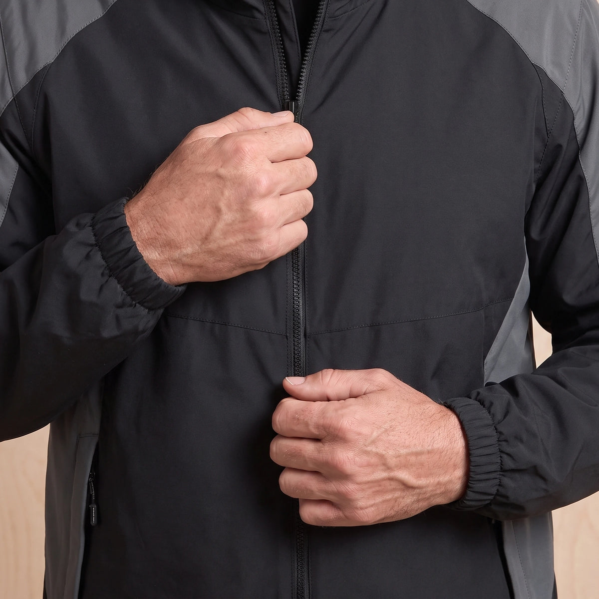 Man zipping up the black hooded panel windbreaker, close view of the front zip and chest