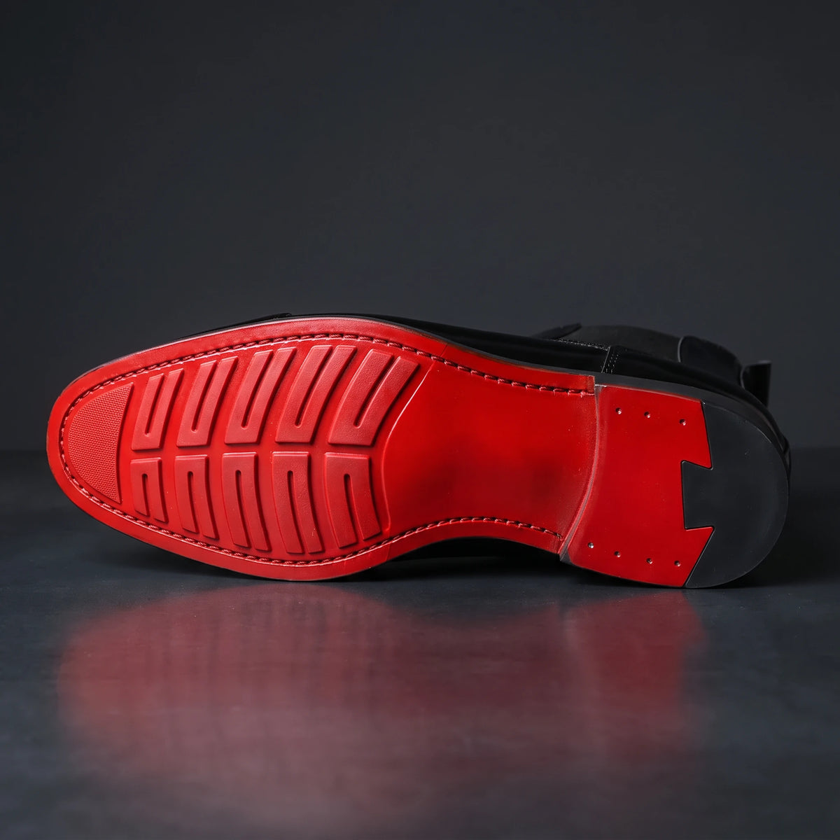 RED SOLE BOOTS macro close-up of the detailed red sole: red lugged forefoot, glossy red waist, black heel with stepped red accent, on dark charcoal