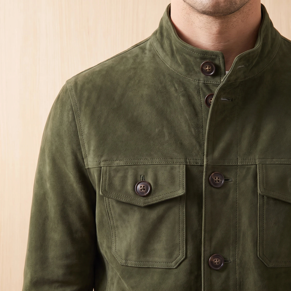 REFINED CHORE JACKET army green suede, close-up of the stand collar, button placket and chest flap pocket on a light bright wood wall