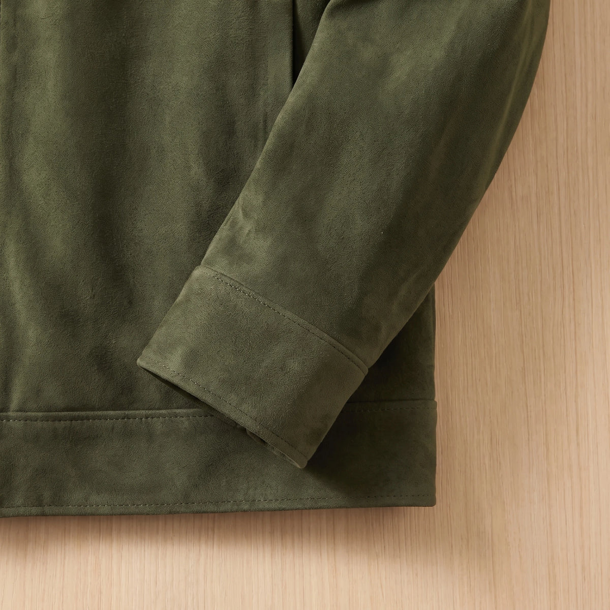 REFINED CHORE JACKET army green suede, close-up of the plain cuff and plain hem with no lower pockets on a light bright wood wall