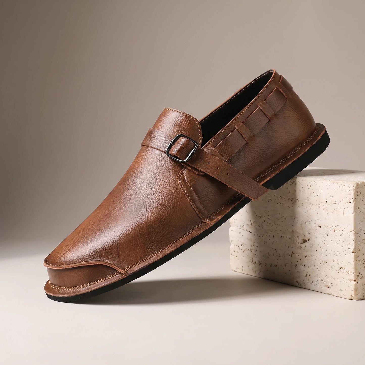 CLASSIC SLIP-ON LOAFERS brown leather slip-on loafer with vamp strap on a travertine studio block