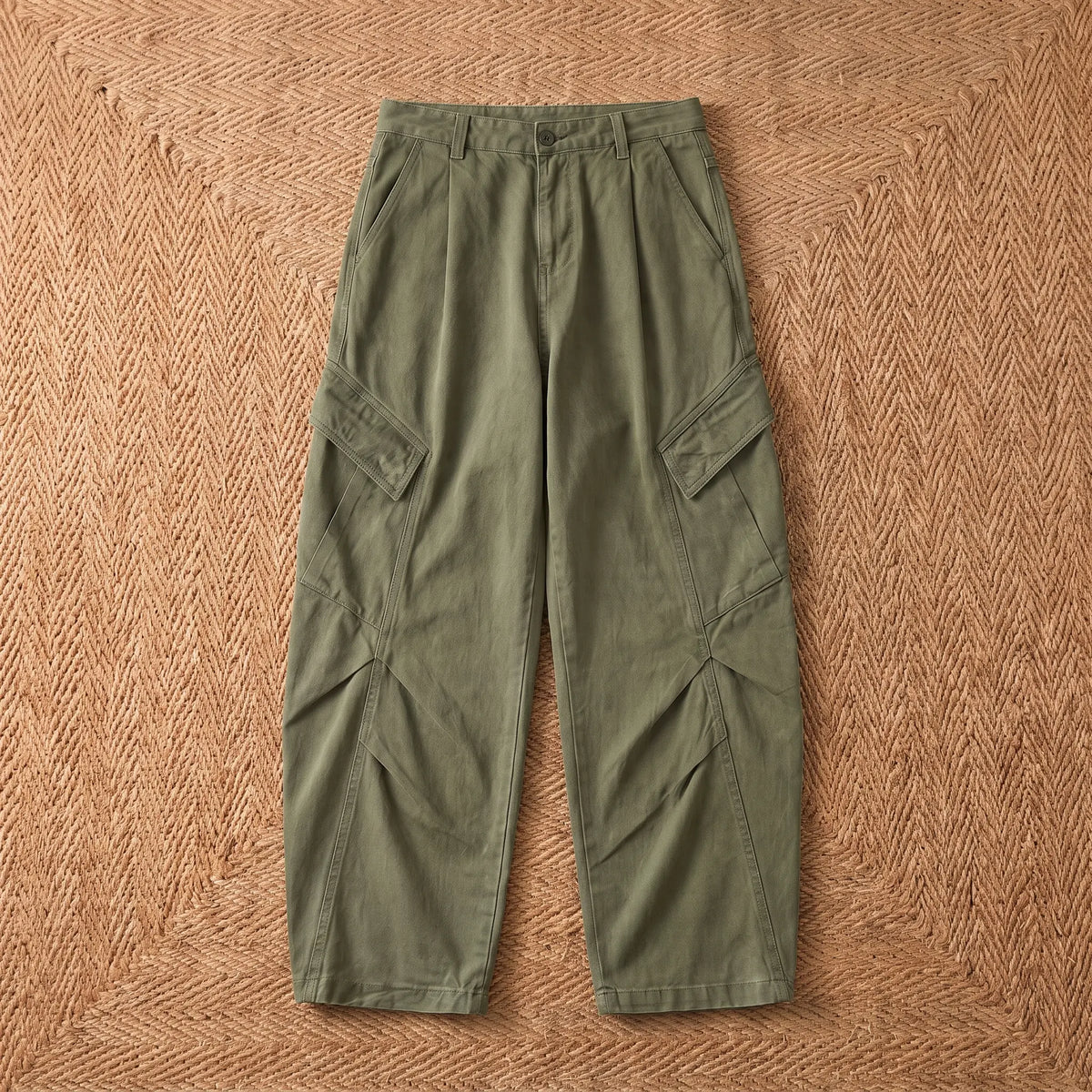 Baggy cargo trousers in washed green cotton laid flat on a jute rug