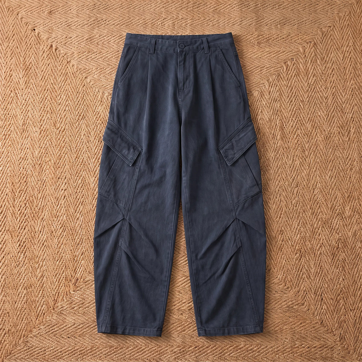Baggy cargo trousers in washed navy blue cotton laid flat on a jute rug