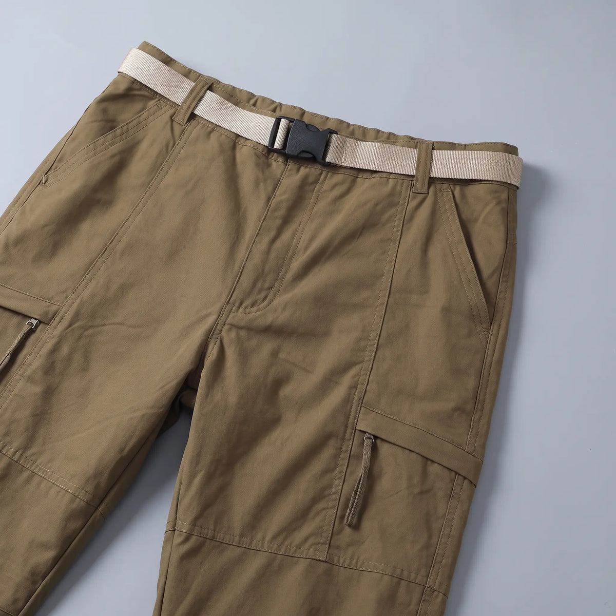 Close up of the BELTED OUTDOOR TROUSERS webbing belt, buckle and zip thigh pocket