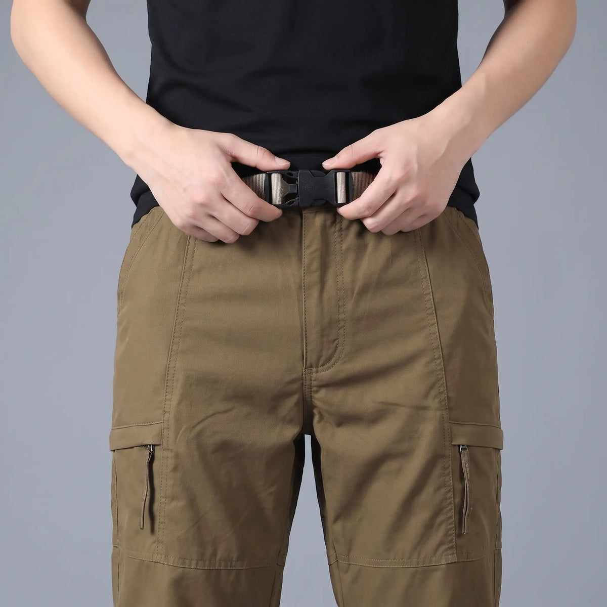 Man fastening the buckle on the BELTED OUTDOOR TROUSERS in brown
