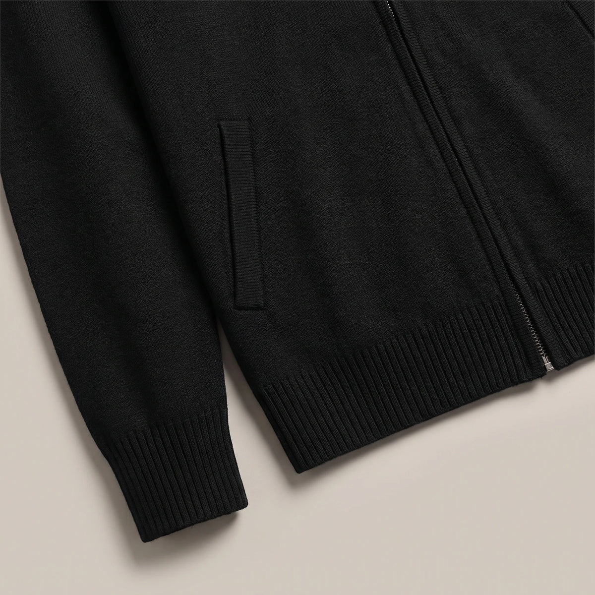 Ribbed cuff, slanted side pocket and ribbed hem of the black knit cardigan laid flat