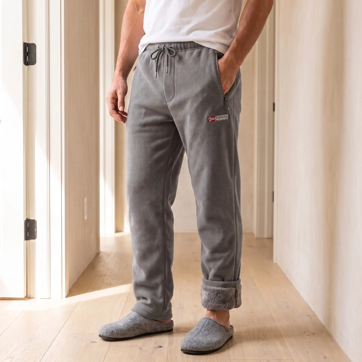 Men's grey sherpa-lined fleece trousers with drawcord waist and rolled cuffs, worn with slippers in a bright hallway
