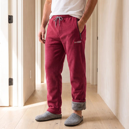 Men's red sherpa-lined fleece trousers with drawcord waist and rolled cuffs, worn with slippers in a bright hallway