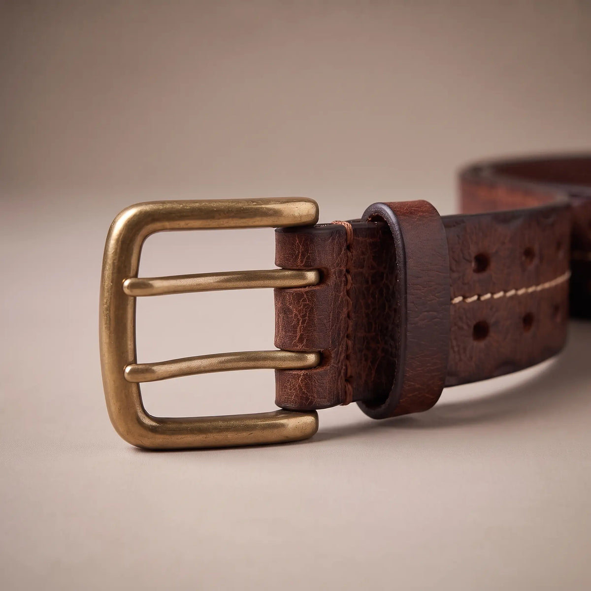 Close-up of the double-prong brass buckle on the brown center stitch leather belt