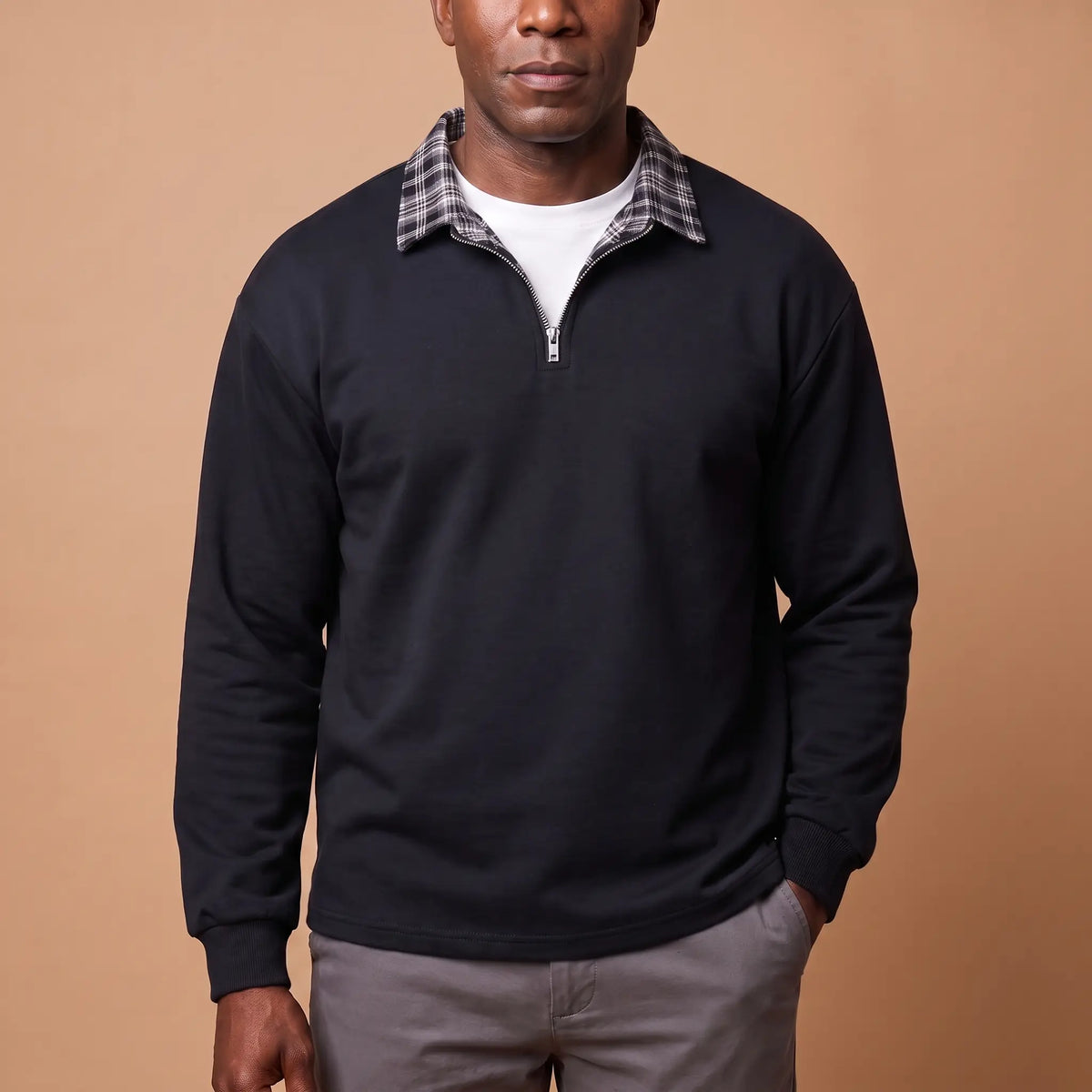 Man wearing black half-zip sweatshirt with check shirt collar and grey chinos
