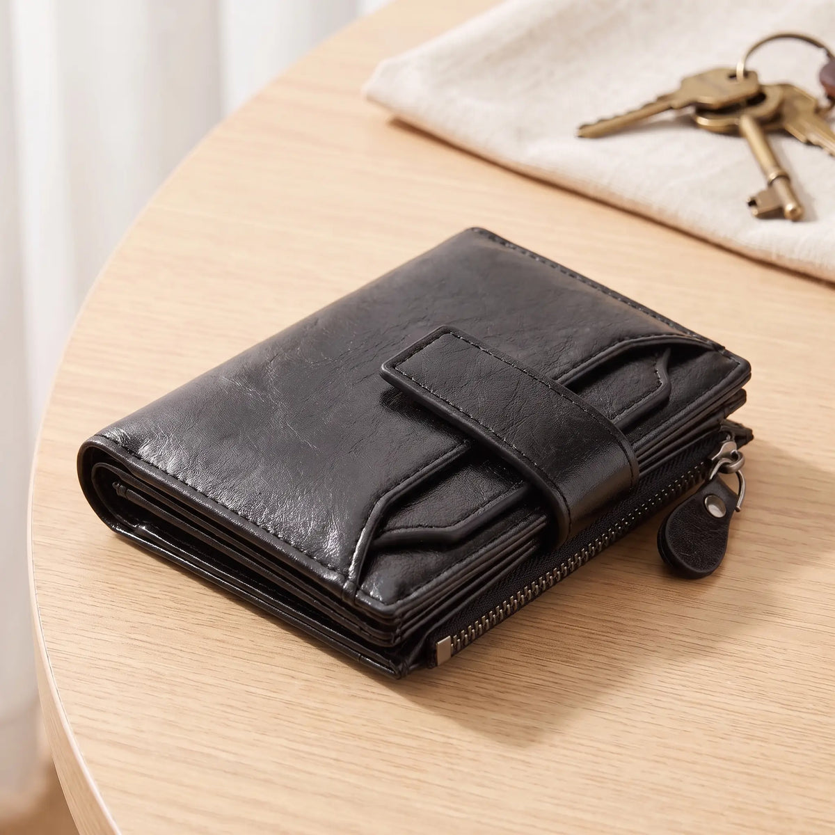 Men's black strap tab bifold wallet with zip coin pocket on an oak table