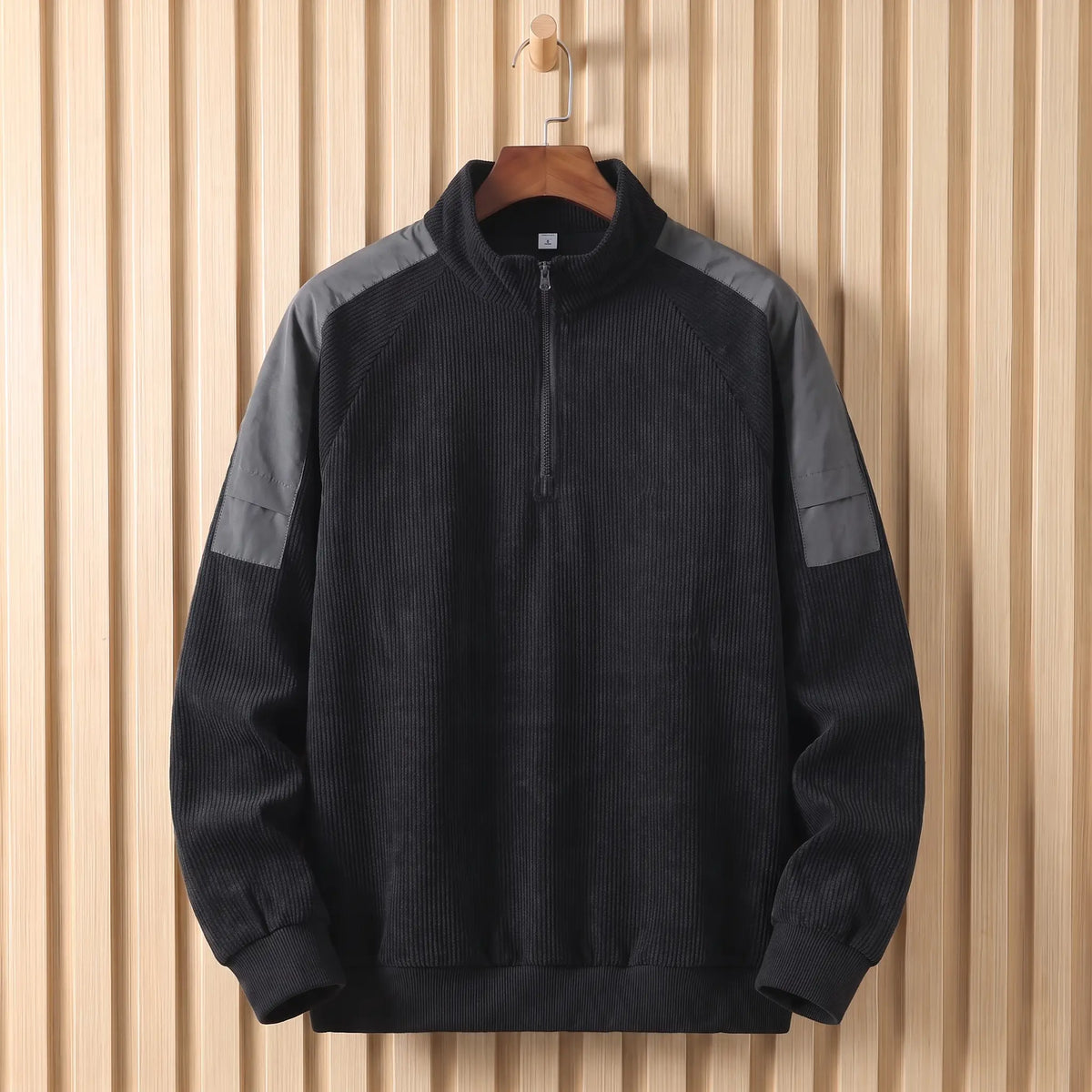 Men's black corduroy quarter-zip sweatshirt with grey shoulder panels on a wooden hanger