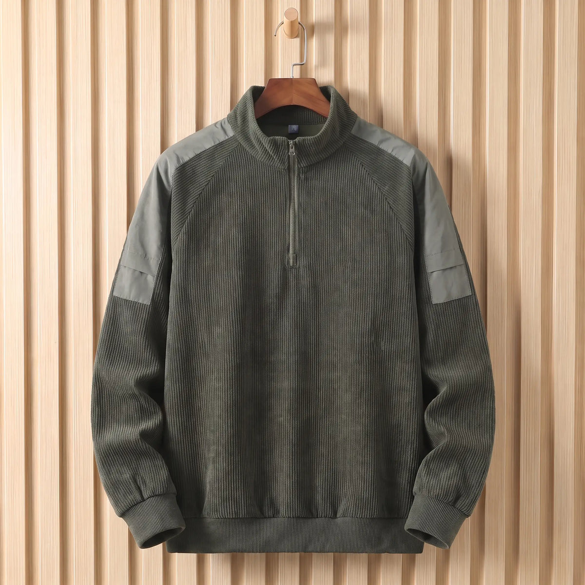Men's army green corduroy quarter-zip sweatshirt with grey shoulder panels on a wooden hanger