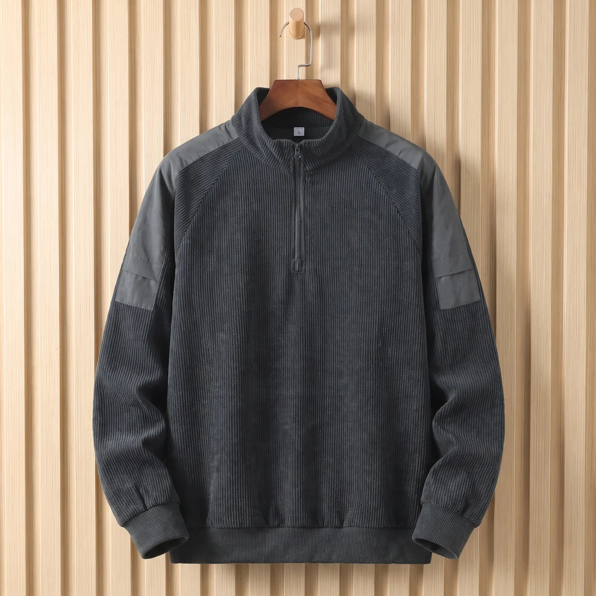 Men's dark grey corduroy quarter-zip sweatshirt with nylon shoulder panels on a wooden hanger