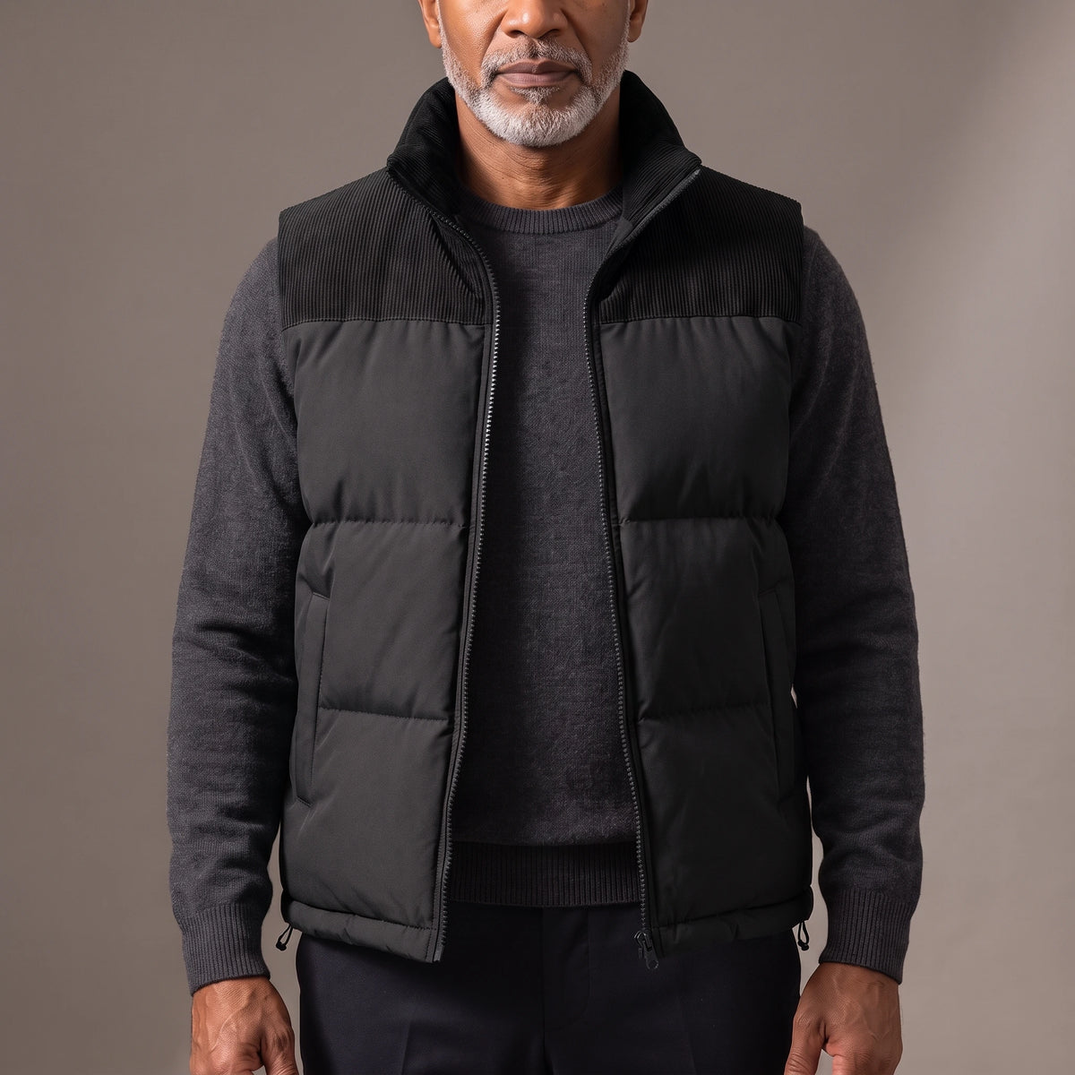 Men's black quilted puffer vest with ribbed cord collar and shoulder yoke, worn open over a charcoal knit