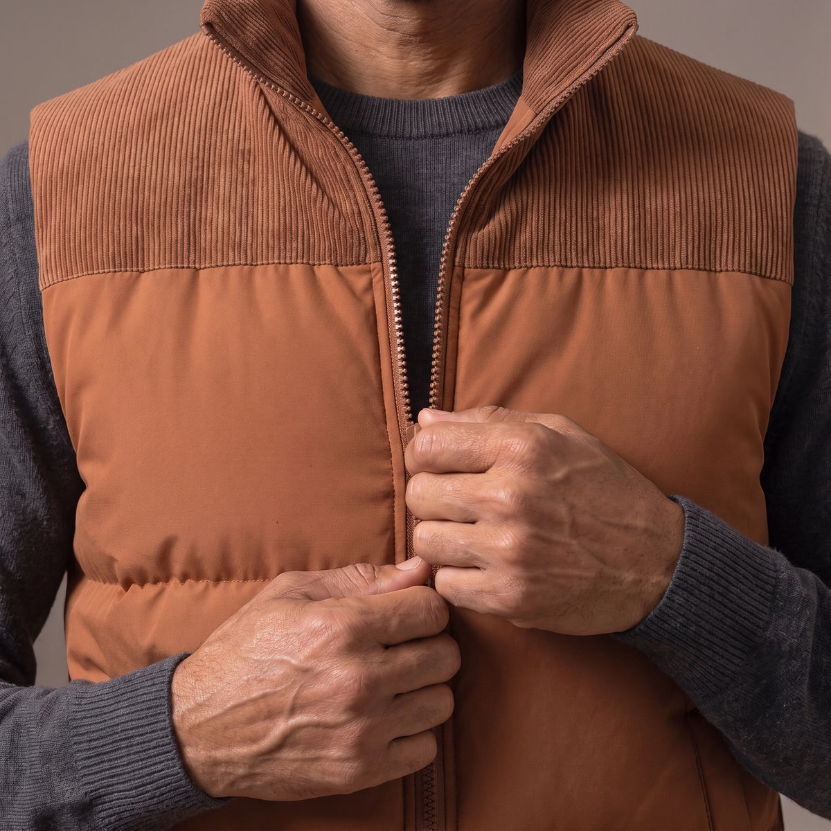 Man zipping up the brown cord yoke puffer vest over a charcoal knit