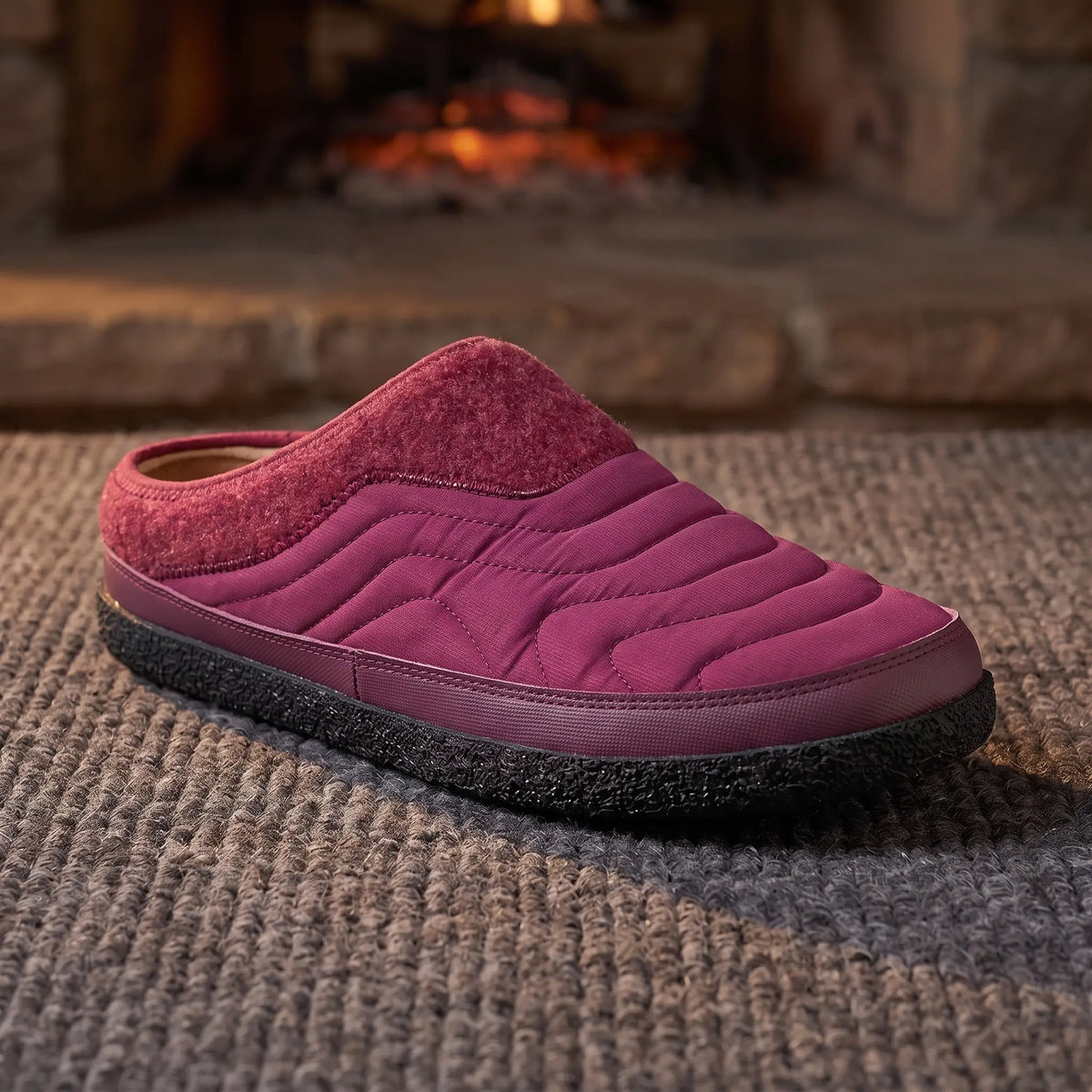 Men's red quilted backless slipper with felt collar and dark speckled sole on a wool rug by a fireplace
