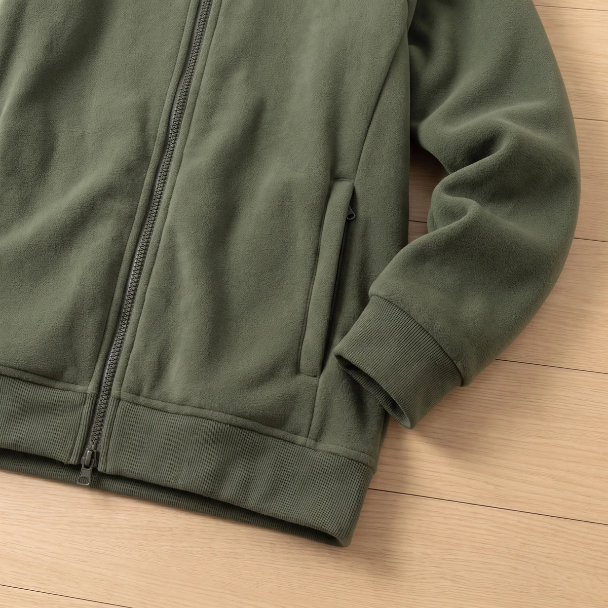 Close-up of green fleece jacket zip pocket, ribbed cuff and hem