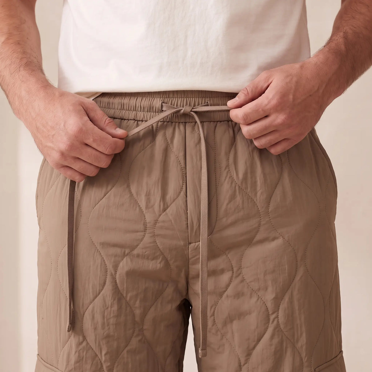 Man tying the drawcord on the COSY QUILTED TROUSERS in brown