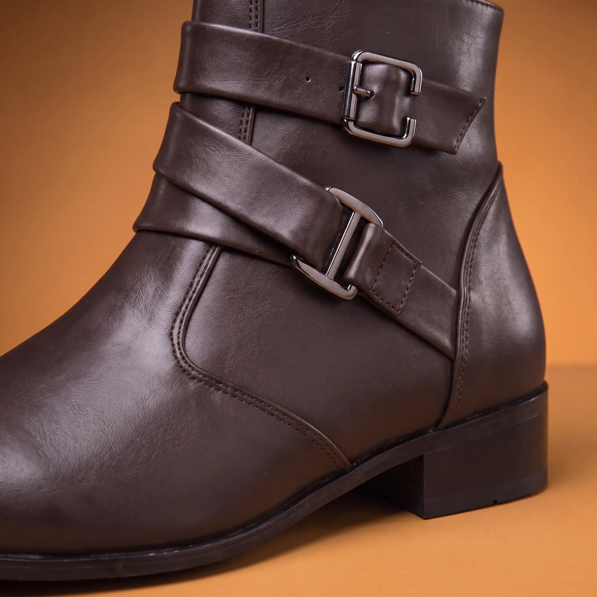 Close up of the crossed ankle straps and twin square buckles on a brown mens boot