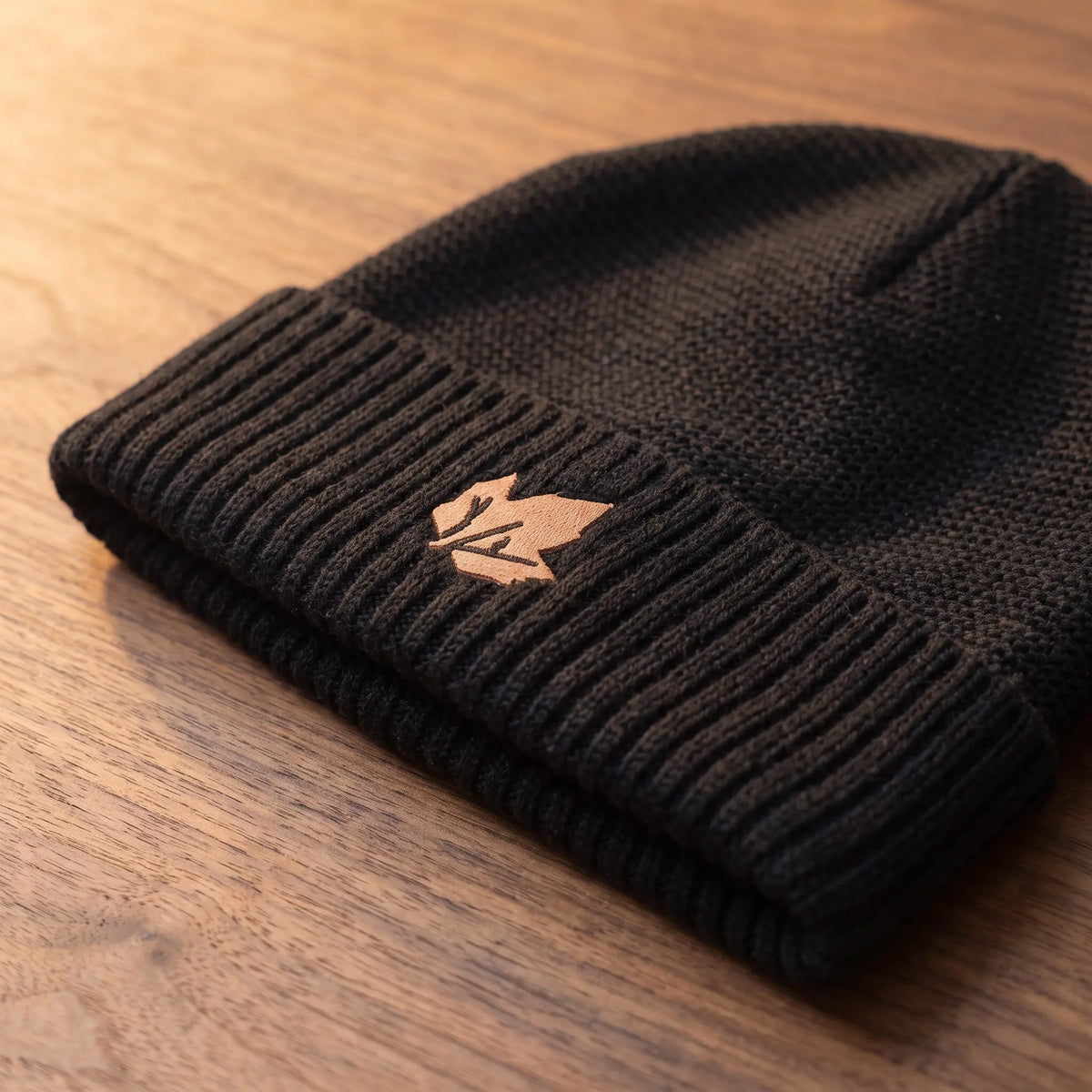 Close up of the ribbed cuff and embroidered badge on the black knit beanie