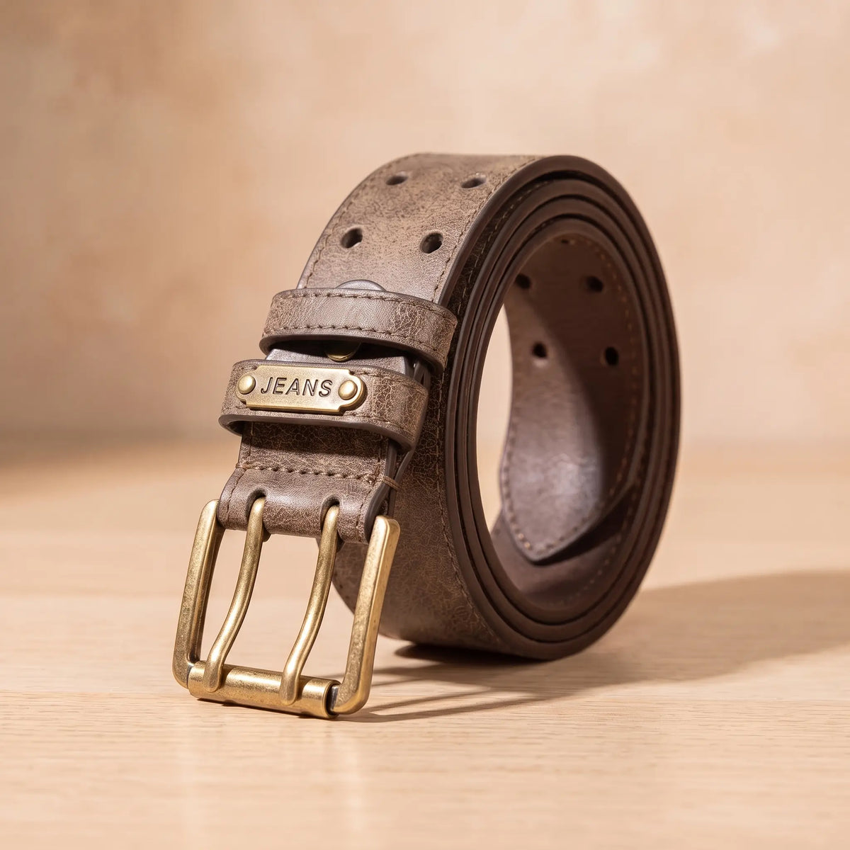 DOUBLE PIN BELT in brown, aged finish belt with antique brass double prong buckle, coiled on light oak