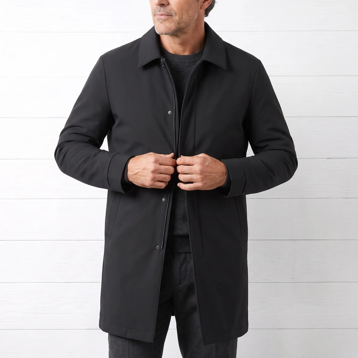 Man buttoning a black down lined coat over a grey knit and charcoal trousers
