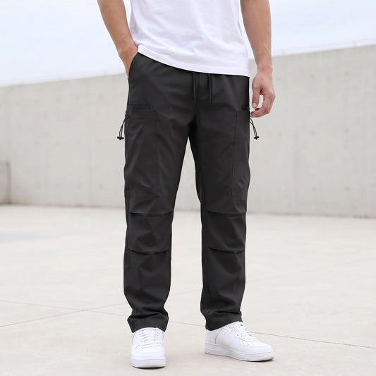 Men's black drawcord cargo trousers worn with a white tee, relaxed straight leg with thigh pockets and pleated knees