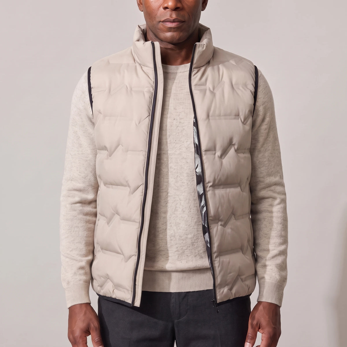Men's beige duck down vest with stand-up collar, worn open over an oatmeal sweater