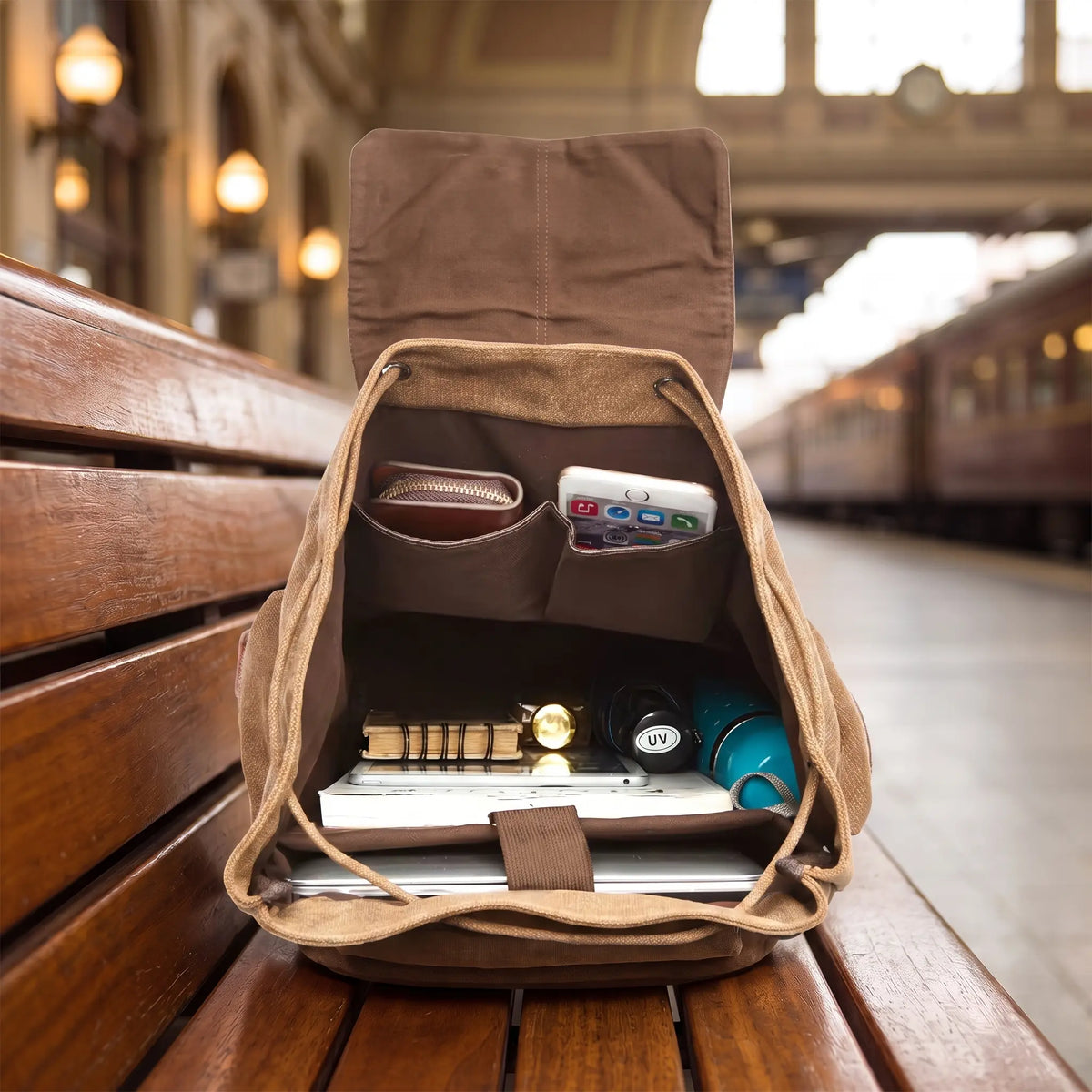 Explorer Canvas Backpack open interior - slip pockets, laptop sleeve, notebook and travel items on a station bench