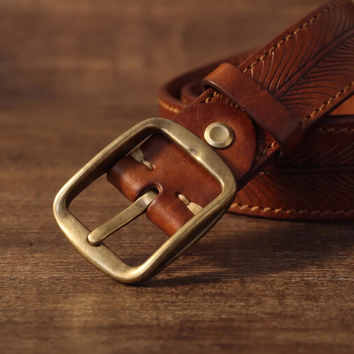 Close-up of the antique brass single-prong buckle on the tan feather embossed belt