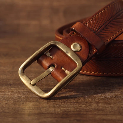 Close-up of the antique brass single-prong buckle on the tan feather embossed belt